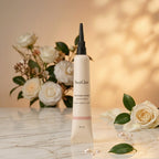 A tube of SaveGlow Radiance Serum stands on a light marble surface with white roses and green leaves in the background, creating a soft, warm, and natural aesthetic.
